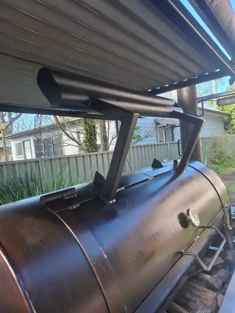 Bertha, the Smoked by Miles offset smoker, with her chimney, firebox and a stack of wood underneath
