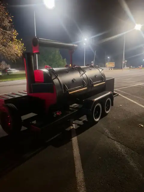 Big Black Betty, a black and red 500 gallon trailer smoker with a tall chimney, parked at night