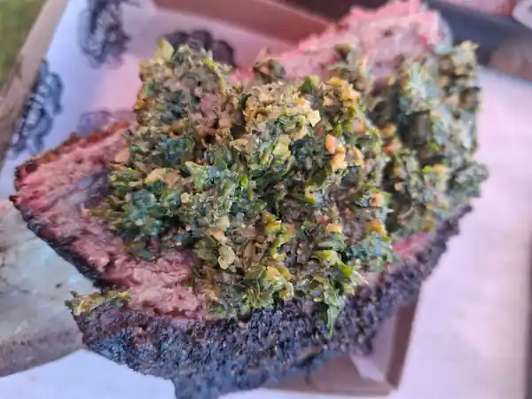 Sliced smoked beef short rib with a dark peppery bark, topped with chimichurri